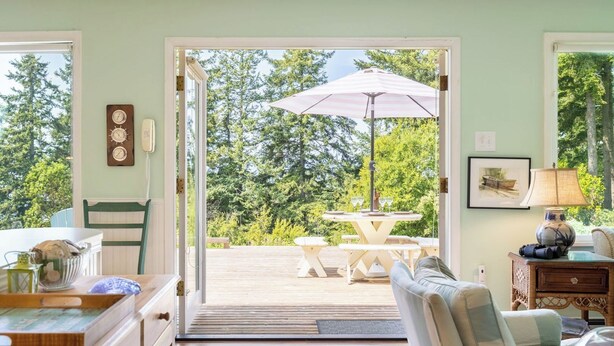 A room with a wooden deck, a table with chairs, a large umbrella, and a chair.