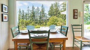 A dining area with a table set for four, surrounded by chairs, with a view of trees and a clear sky.