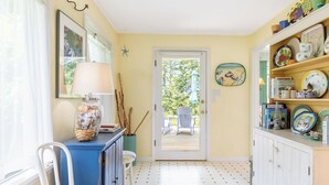 A kitchen with a blue cabinet, a white chair, a door leading to an outdoor deck, and shelves with dishes and books.
