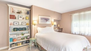 Un dormitori amb un llit gran, una estanteria, un escriptori i una finestra amb cortines.