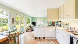 A kitchen with white cabinets, a dining area with a table and chairs, and a view of the outdoors.