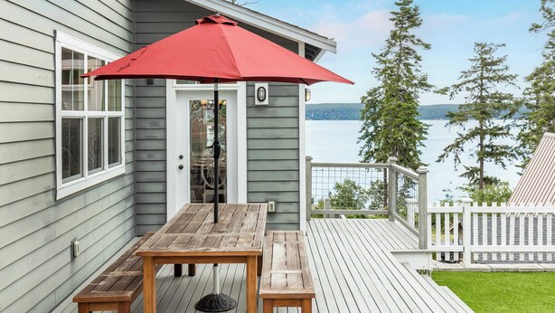 Une terrasse en bois avec un parasol rouge, une table et un banc.
