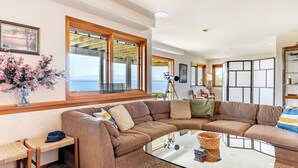 A modern living room with a large sectional sofa, a glass coffee table, and a view of the sea through large windows. - The Majestic Blue View by Avantstay Waterfront (Freeland)