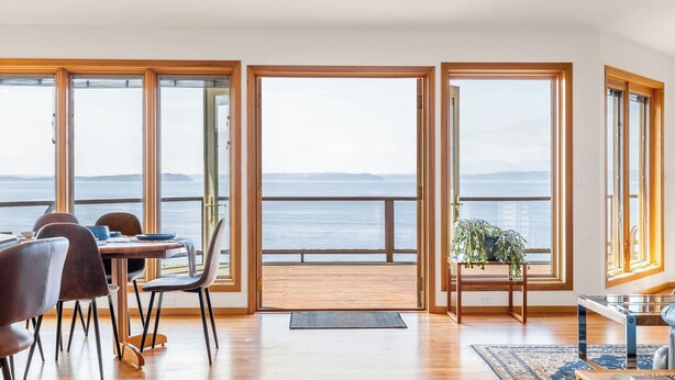 A dining area with a view of the sea, large windows, and a potted plant. - The Majestic Blue View by Avantstay Waterfront (Freeland)