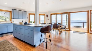 A modern kitchen with a central island, large windows, and a view of the sea. - The Majestic Blue View by Avantstay Waterfront (Freeland)