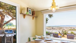 Comedor con vista a la playa, una parrilla y una mesa de madera dispuesta para dos.