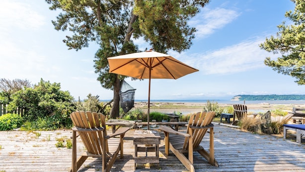 Una terraza de madera con una mesa, sillas y una sombrilla, con vistas a la playa y al océano.