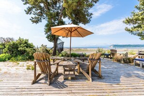 A wooden deck with a table and chairs, an umbrella, and a view of the beach and ocean. - Sunlight Beach Getaway by Avantstay Views (Clinton)