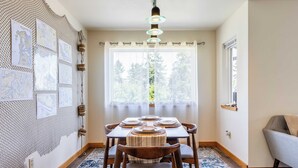 A dining area with a table set for four, a hanging light fixture, and a window with a view of trees.
