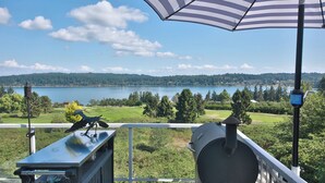 A balcony with a view of a lake, a bird sculpture, and a closed umbrella. - Fairway Harbor View by Avantstay Outdoor Oasis (Freeland)