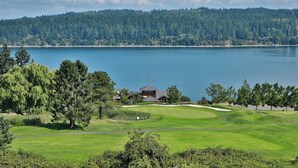 A golf course with a clubhouse, surrounded by dense forest and a large body of water. - Fairway Harbor View by Avantstay Outdoor Oasis (Freeland)