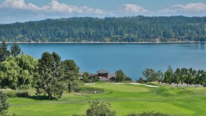 Un campo de golf con un club de campo, un lago y una colina boscosa al fondo.