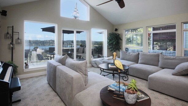 A spacious living room with a piano, large windows, a ceiling fan, and a view of a sailboat. - Fairway Harbor View by Avantstay Outdoor Oasis (Freeland)