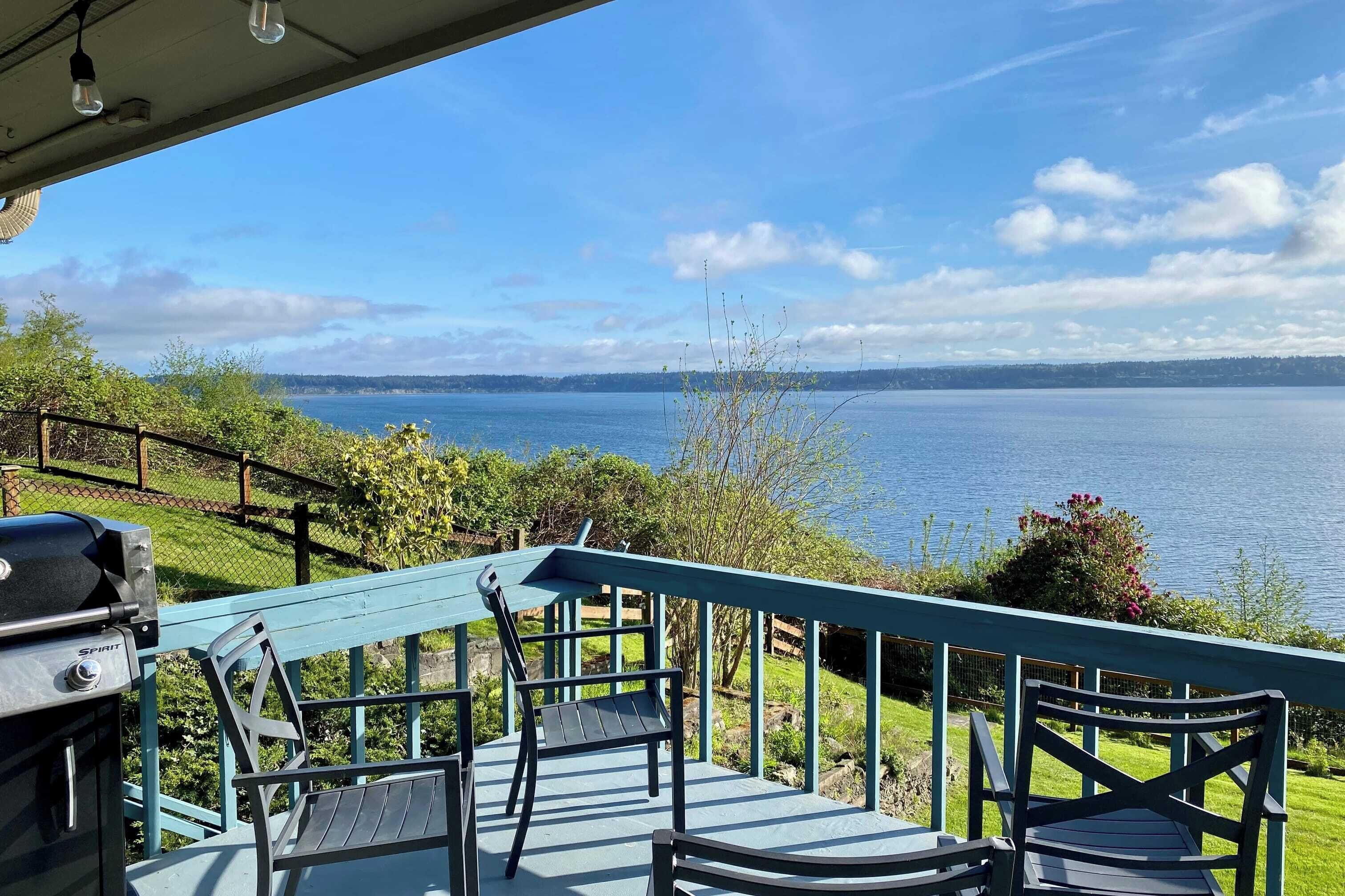 A deck with a grill and chairs overlooking a lake.