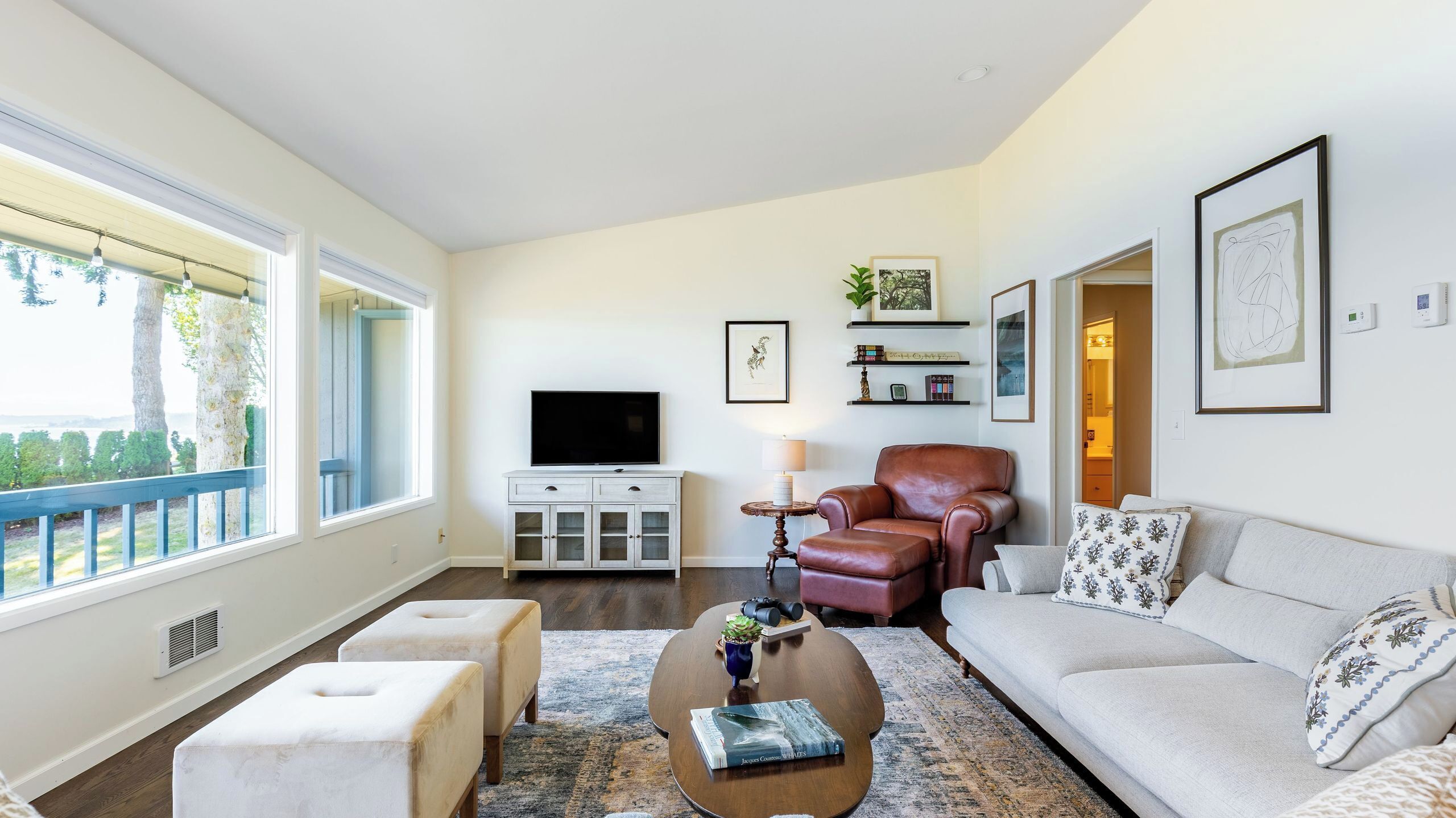 A living room with a sofa, ottomans, a coffee table, a TV, and a bookshelf.