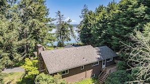 A two-story house with a sloped roof, surrounded by dense forest and a lake view. - Eagles Watch by Avantstay Large Deck w/ Views (Coupeville)