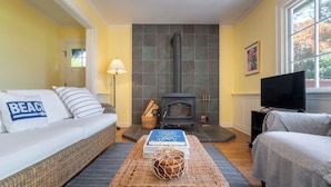 A living room with a sofa, a television, a fireplace, and a bookshelf. - Smugglers Lagoon Beach Cottage by Avantstay (Greenbank)