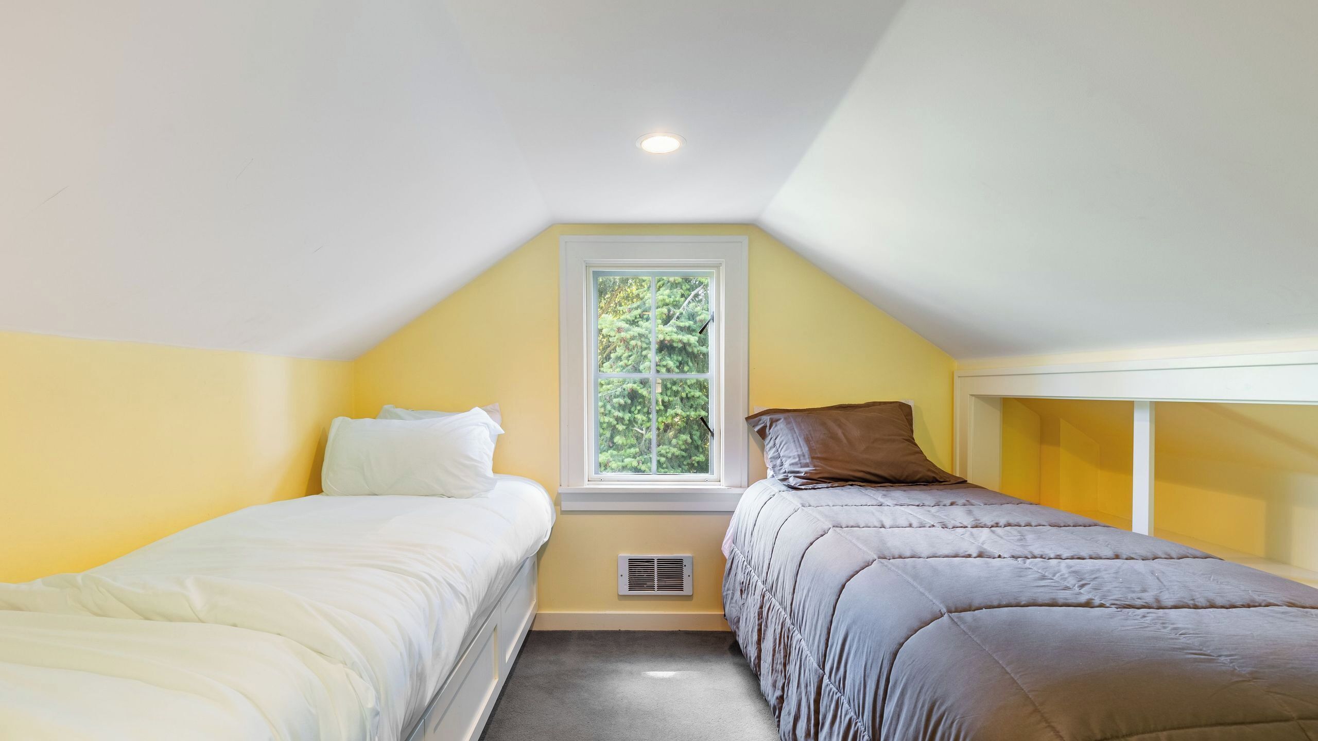 A bedroom with two beds, a window with a view of trees, and a ceiling vent.
