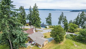 Une propriété résidentielle comprenant une maison, un garage et une allée, le tout entouré d’arbres et offrant une vue sur un lac.