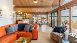 A modern interior with a wooden ceiling, a leather sofa, a patterned armchair, and a view of the sea through large windows. - Oceanfront w/ Game Room, Fire Pit, Panoramic Views Angels Landing by Avantstay (Langley)