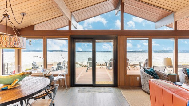 A spacious room with a wooden ceiling, large windows, a dining area, and a seating area with a view of the water. - Oceanfront w/ Game Room, Fire Pit, Panoramic Views Angels Landing by Avantstay (Langley)