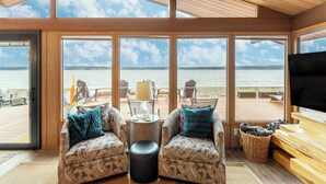 A cozy room with large windows overlooking a body of water, furnished with patterned sofas and a television. - Oceanfront w/ Game Room, Fire Pit, Panoramic Views Angels Landing by Avantstay (Langley)