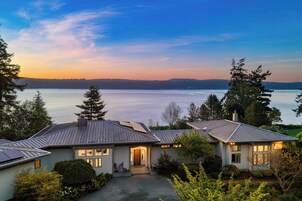 A two-story house with a view of a lake, surrounded by trees and a well-maintained lawn.