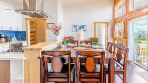 A modern kitchen with a central island, wooden chairs, and a dining table set for four. - Chateau Coho by Avantstay Easy Beach Access (Greenbank)