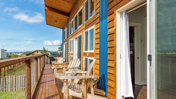 A wooden deck with Adirondack chairs, a glass door leading to a room, and a view of the ocean. - Chateau Coho by Avantstay Easy Beach Access (Greenbank)