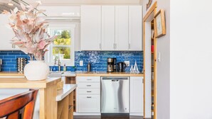 A modern kitchen with white cabinets, a blue backsplash, and a dishwasher. - Chateau Coho by Avantstay Easy Beach Access (Greenbank)