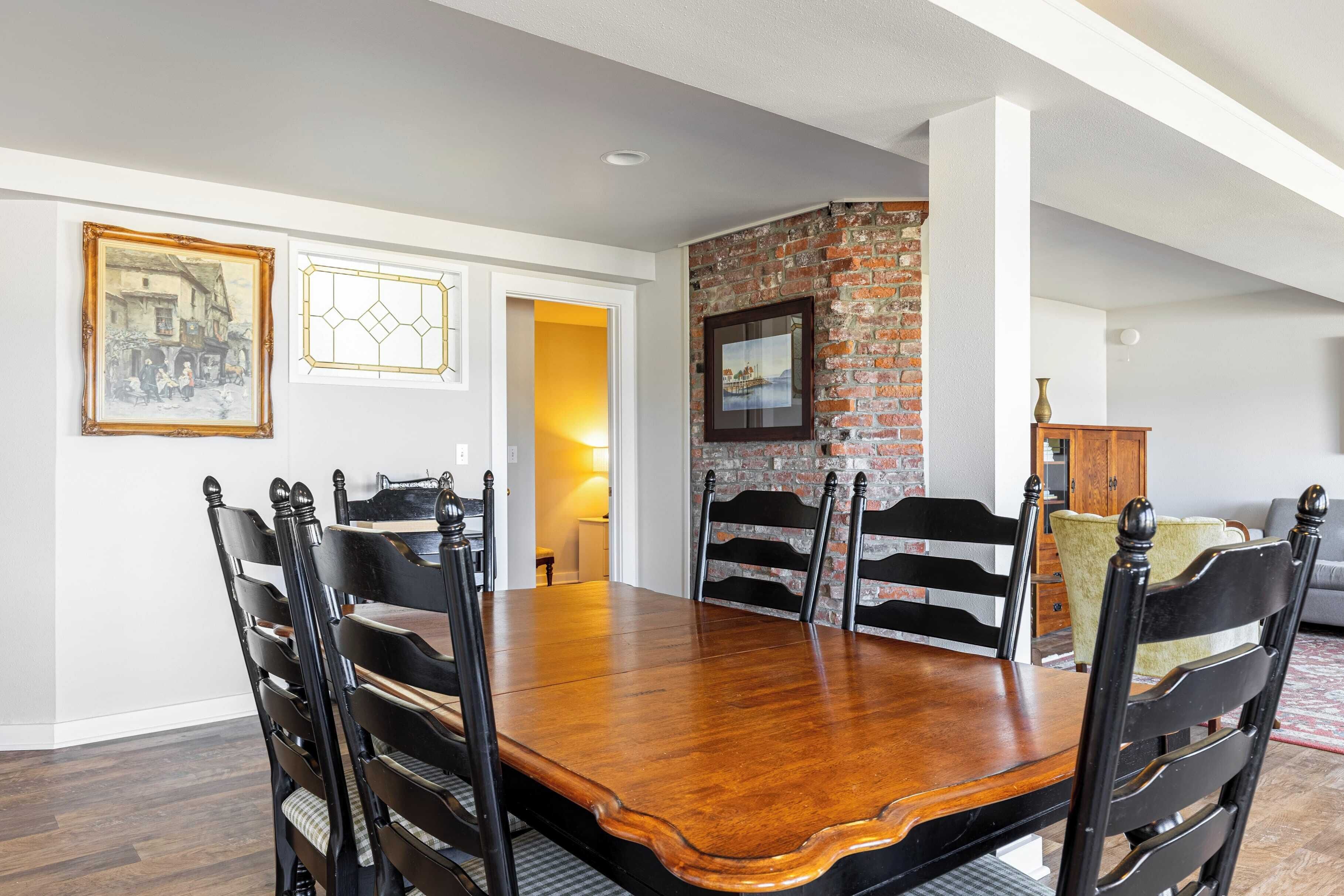 A dining area with a wooden table and chairs, a brick wall, and framed artwork on the walls.