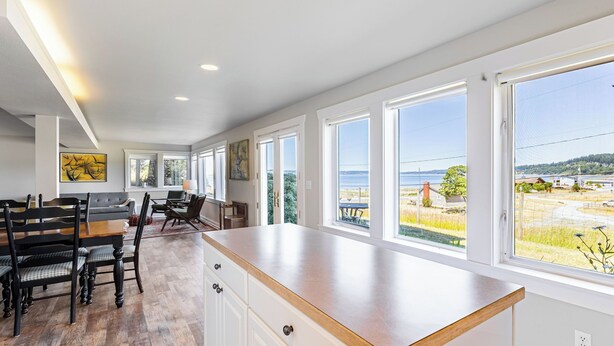 Una cocina amplia con una isla grande, un comedor con sillas y ventanas grandes con vistas al mar.