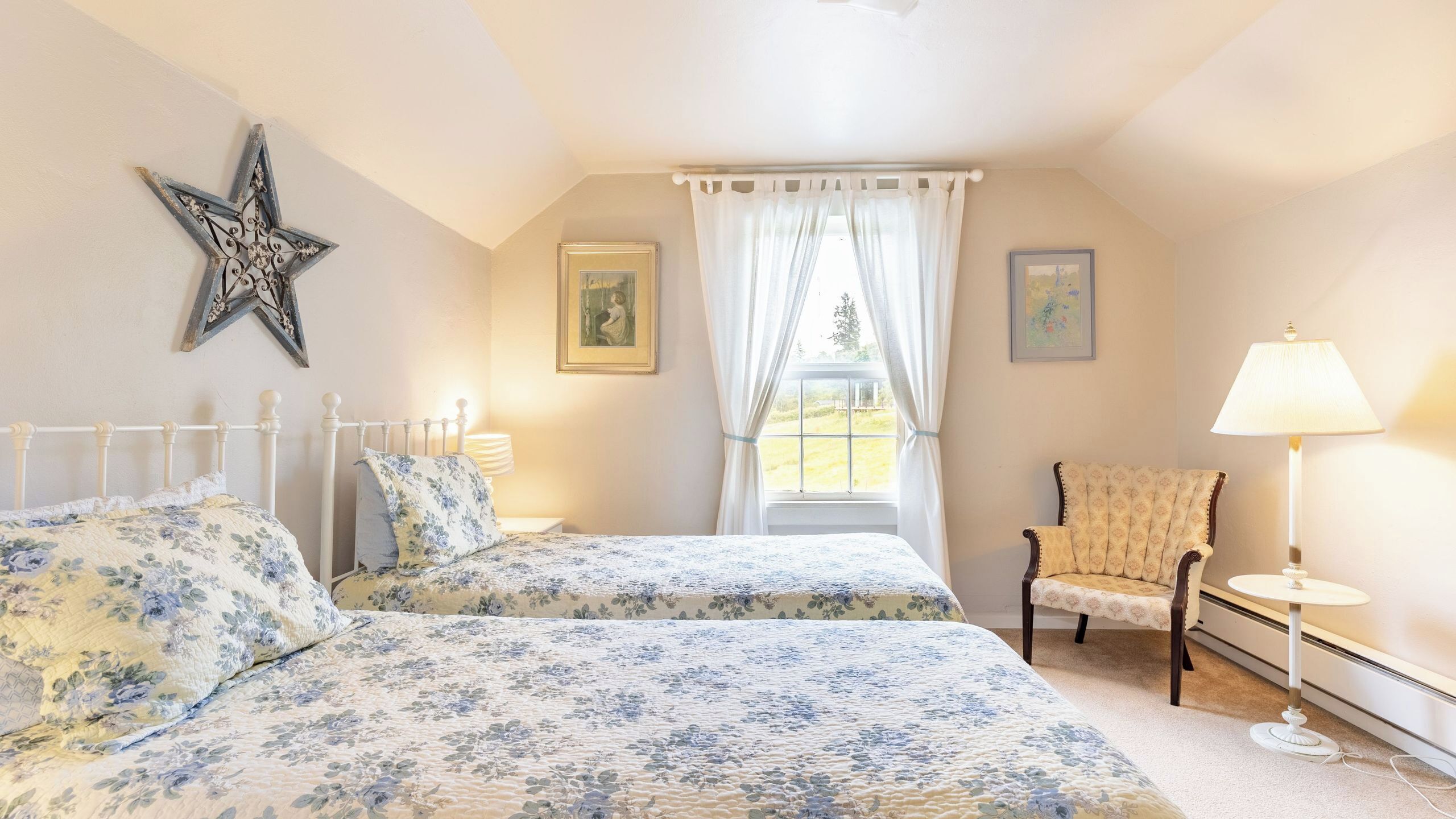 Een slaapkamer met twee bedden, een sterren decoratie, een stoel, een lamp en een raam met gordijnen.