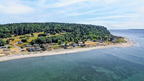 Vista aérea de una zona residencial costera con casas, una playa y una colina boscosa.