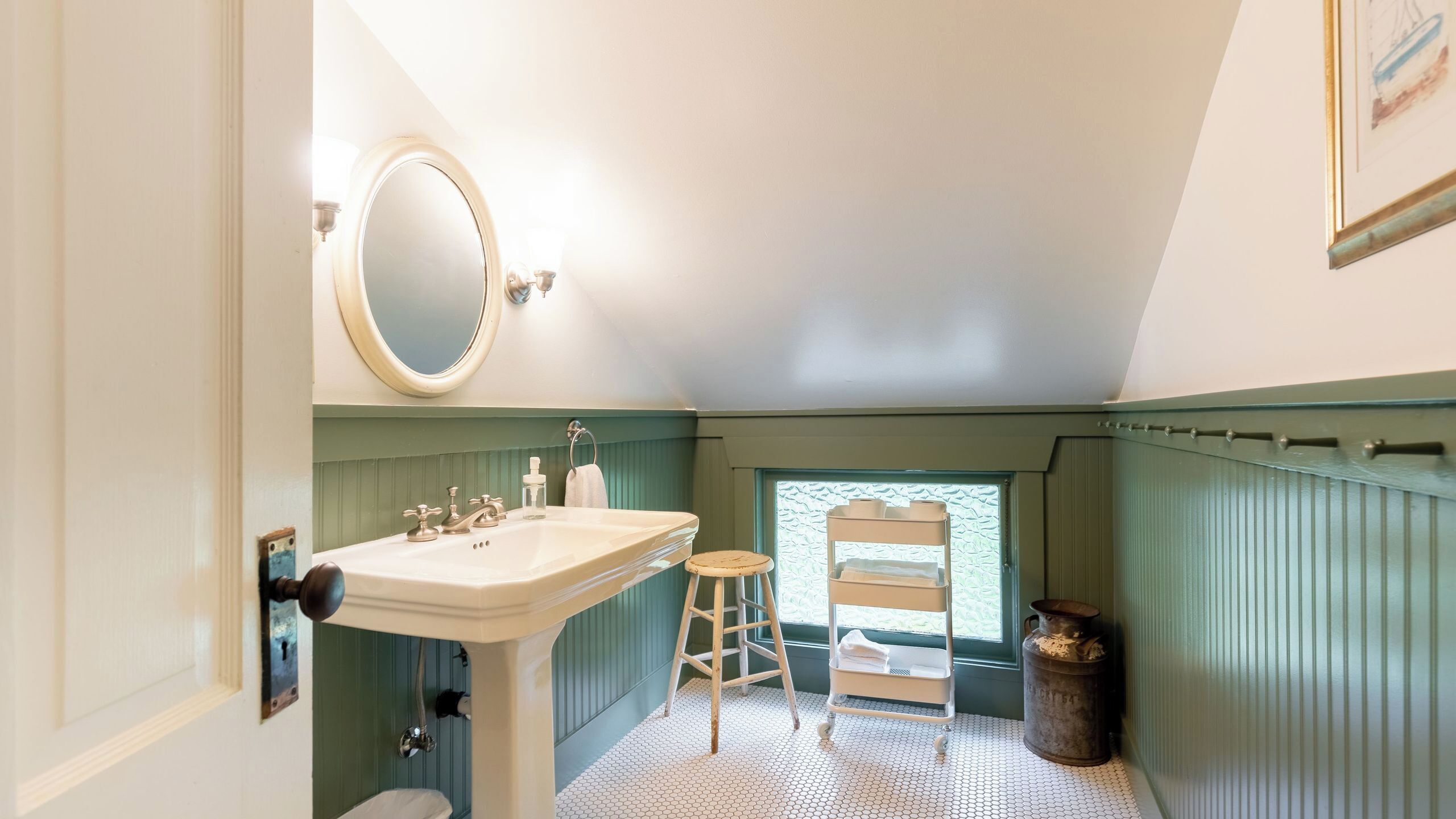 Un bagno con un lavandino bianco, uno specchio rotondo, uno sgabello di legno, una scaletta bianca e un termosifone.