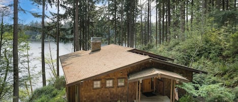 A wooden cabin with a sloped roof, a chimney, and a porch with steps leading to the entrance.