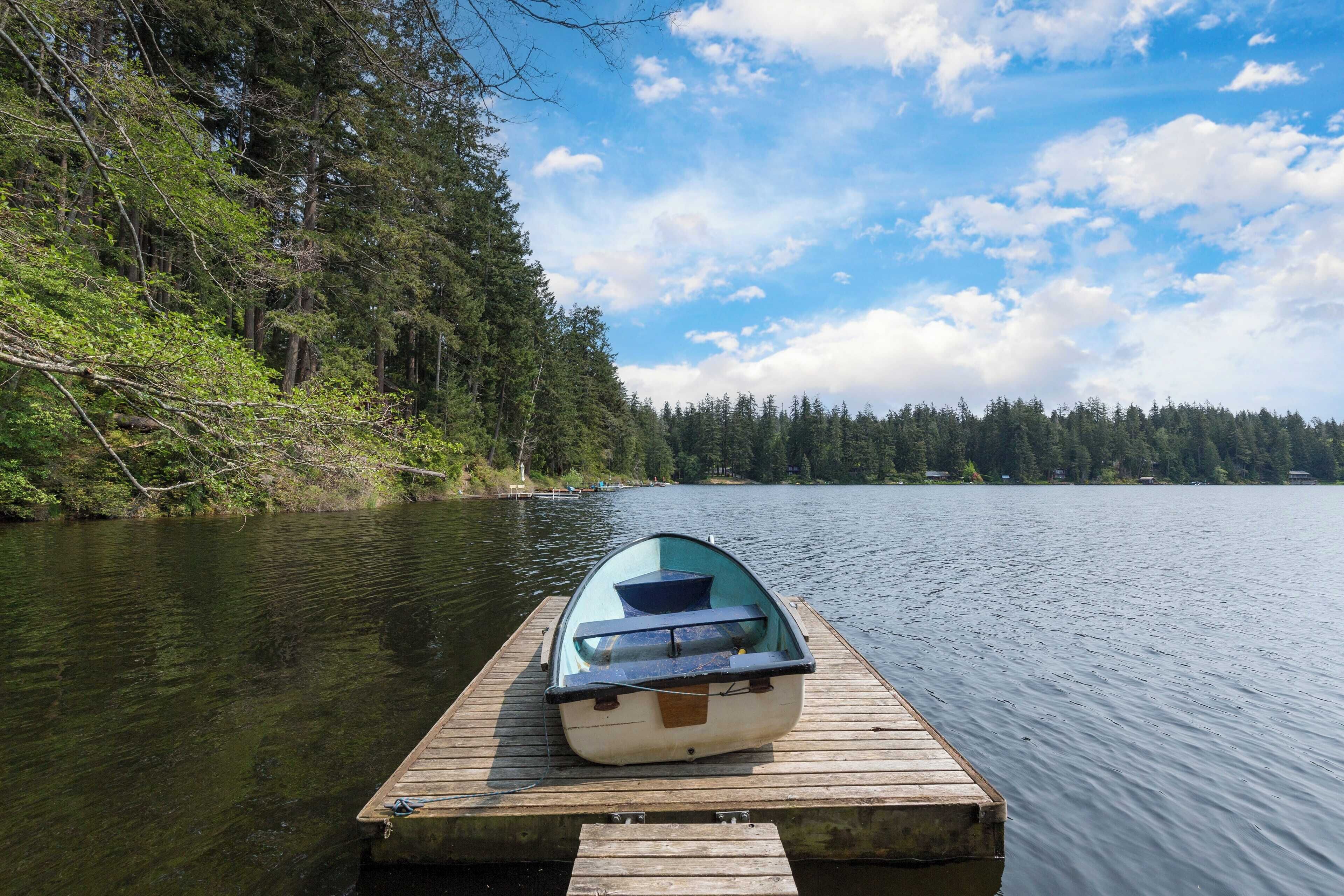 A small boat on a wooden dock extending into a calm lake, surrounded by dense forest.