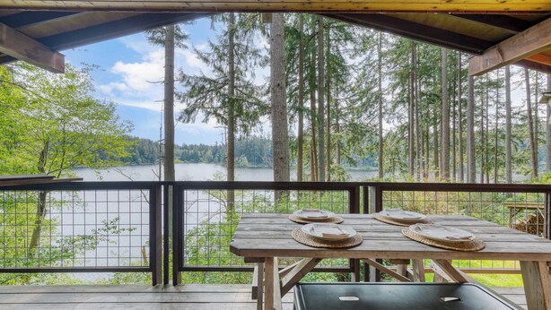 Eine Holzterrasse mit einem Tisch für zwei Personen, mit Blick auf einen von Bäumen umgebenen See.