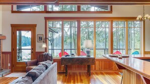 Ein gemütliches Wohnzimmer mit Holzboden, einer Couch, einem Tisch und großen Fenstern mit Blick auf den Wald.