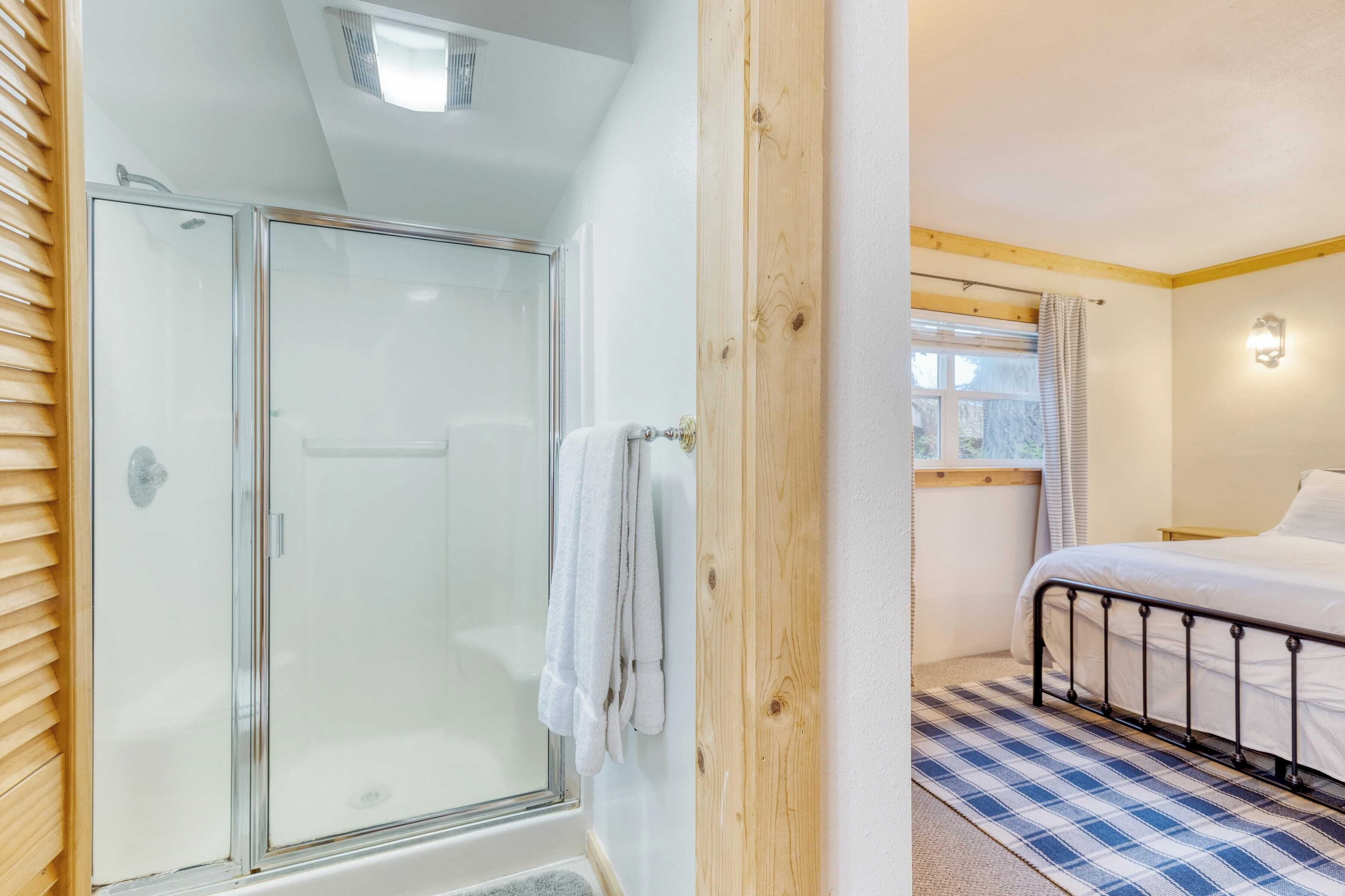 A bedroom with a bed, a window with curtains, a wooden door, and a shower area with a glass door.