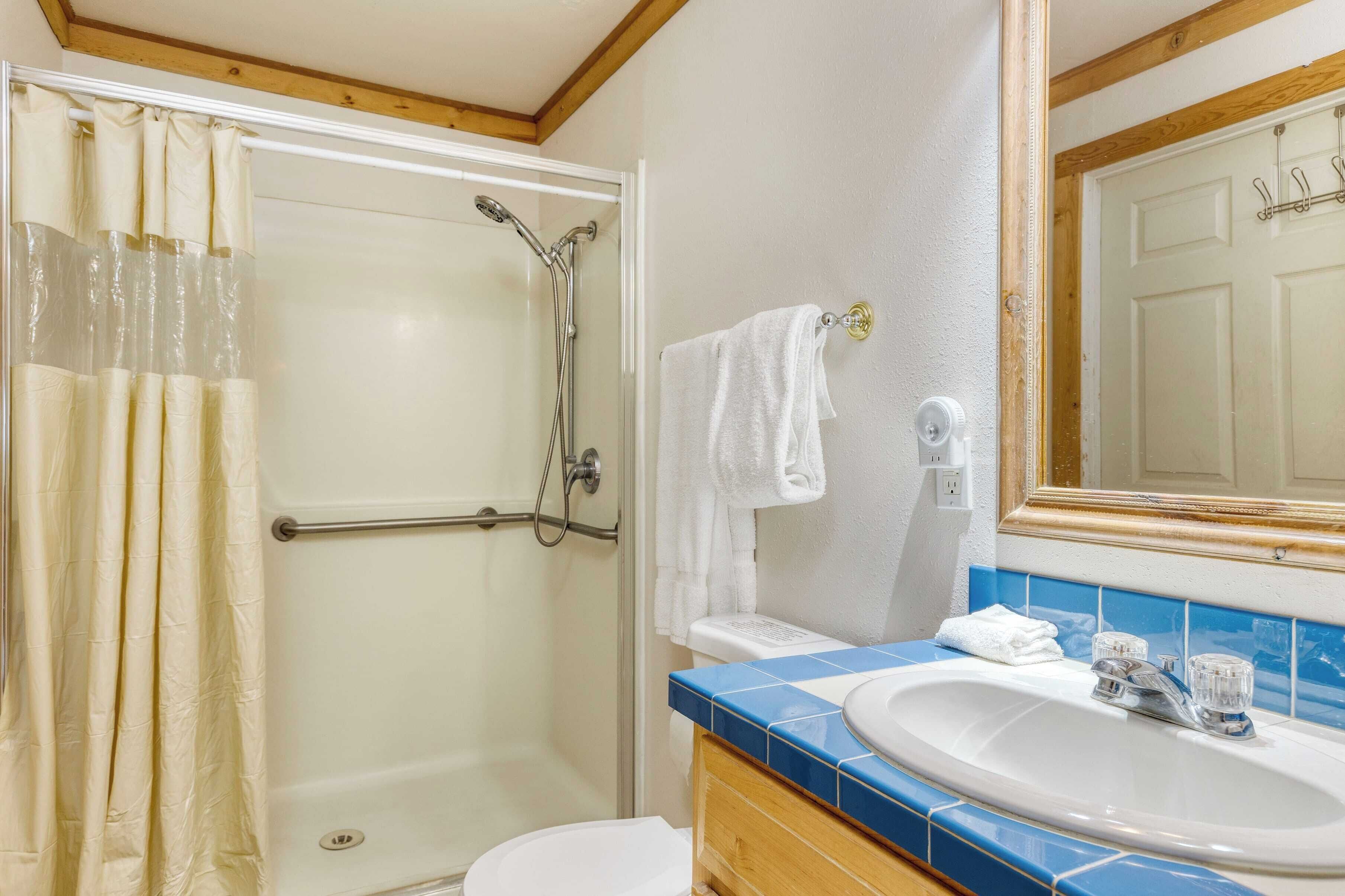 A bathroom with a glass shower enclosure, a white toilet, a sink with blue tiles, and a towel hanging on a rack.