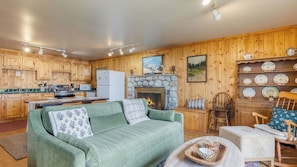 A cozy cabin-style room with a fireplace, wooden walls, a sofa, and a dining table. - Cove Cottage by Avantstay Waterfront Views + Spa (Coupeville)