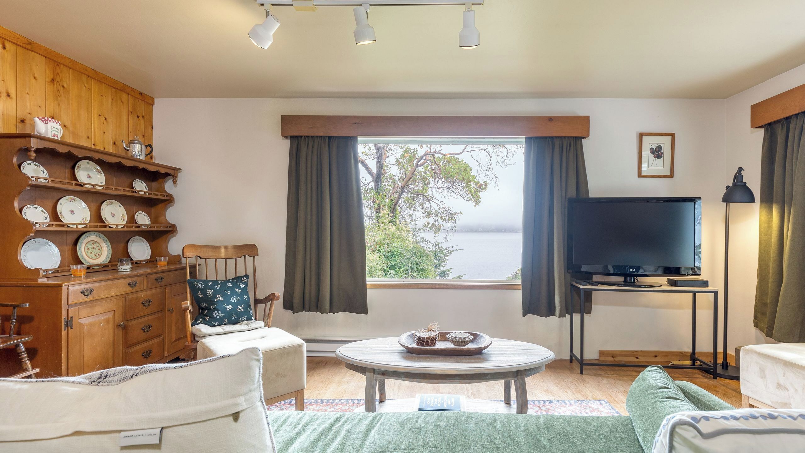 Une pièce avec un meuble en bois, une télévision, une table ronde et une vue sur l’extérieur.