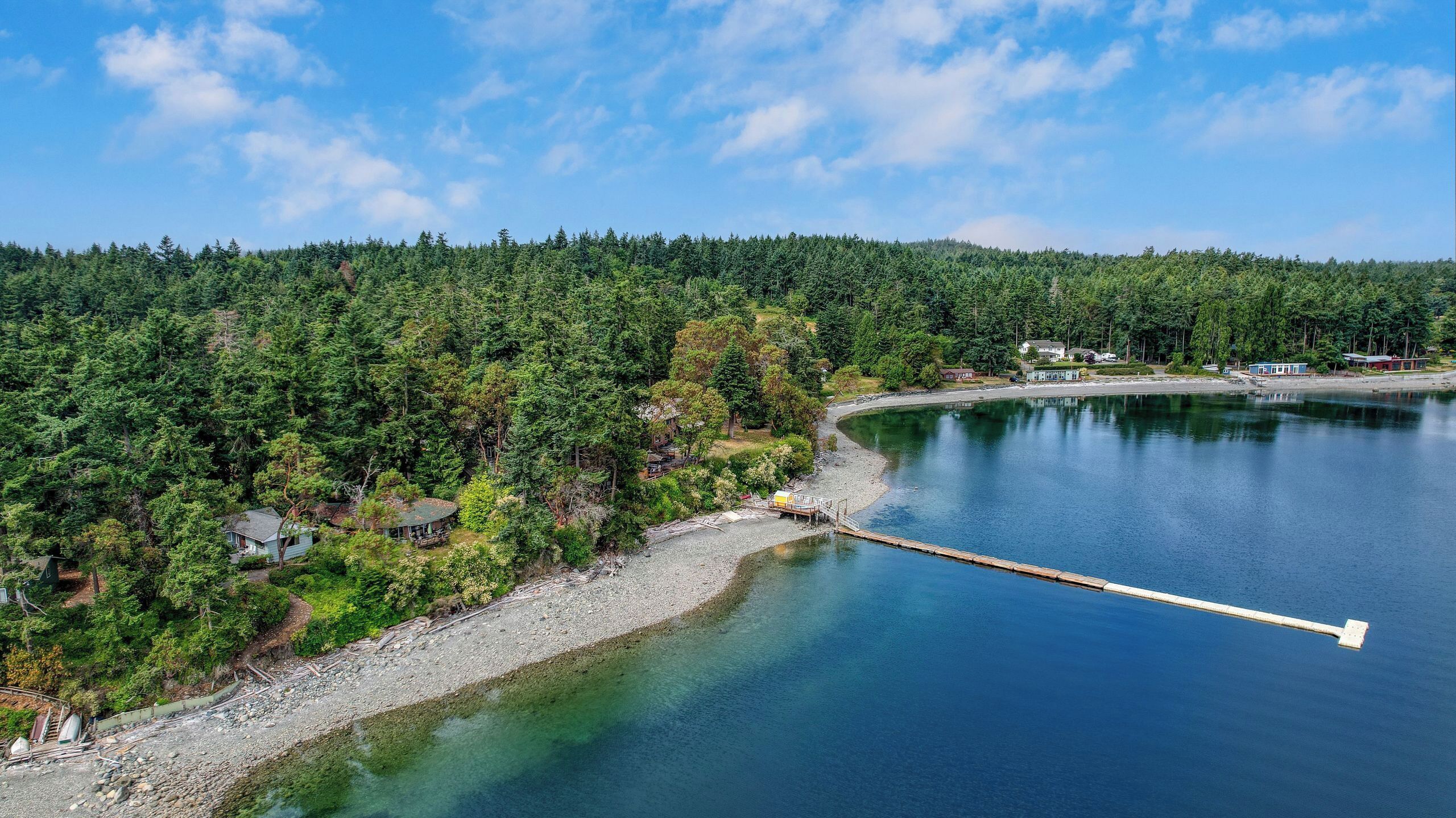 A lakeside property with a dock extending into the water, surrounded by dense forest and a few buildings.