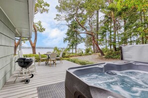 Un bain à remous sur une terrasse en bois, avec vue sur la mer et les arbres.