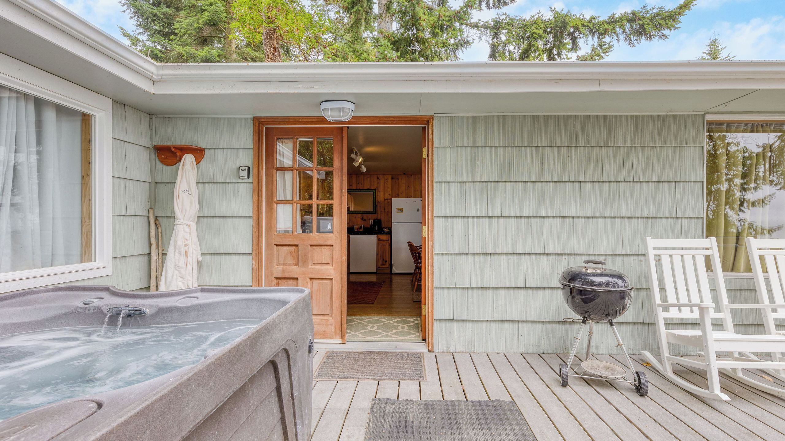 A wooden deck with a hot tub, a grill, and a white chair.