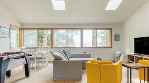 Un salon avec un canapé, des fauteuils jaunes, un téléviseur et une table de baby-foot.