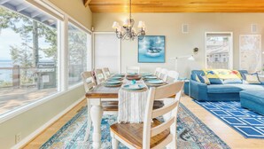 A dining area with a wooden table set for six, a chandelier, and a view of the outdoors. - Barranco by Avantstay Stairway to Beach + Views (Greenbank)
