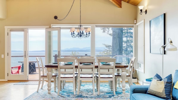 Un coin repas avec une table dressée pour quatre personnes, un lustre et une vue sur l’océan.