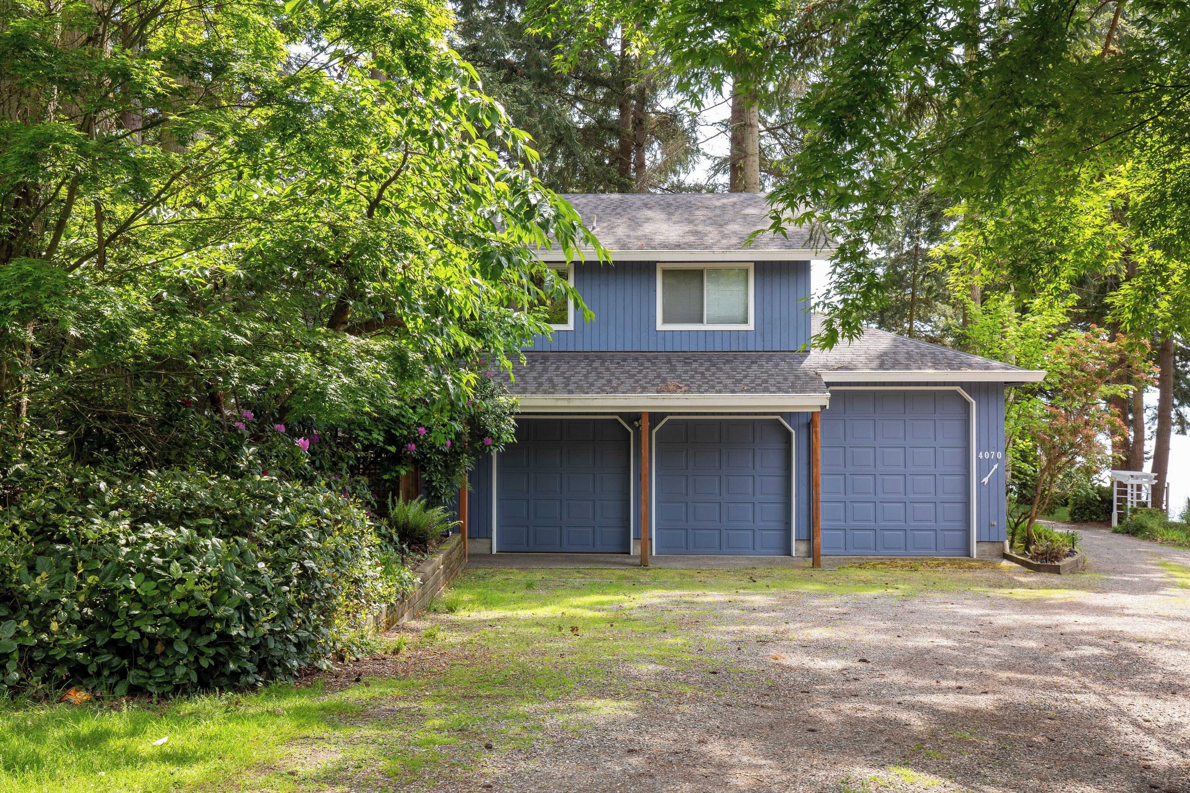 A two-story house with a blue exterior, a covered garage, and a gravel driveway.